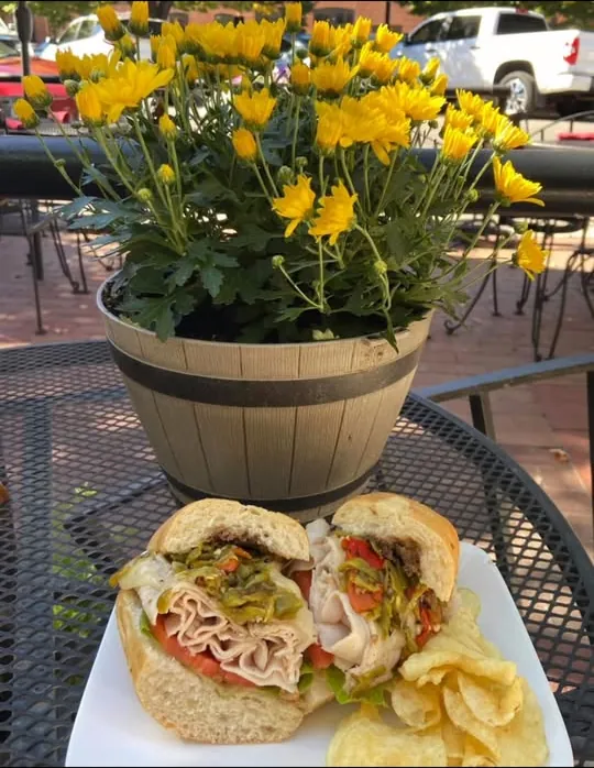 A turkey sandwich with green chiles and tomato and a side of kettle chips on our patio table, next to a pot of yellow mums