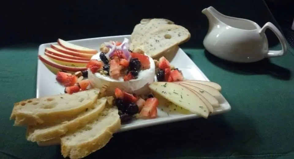 A plate of warm brie with sliced apple, berries and rustic bread